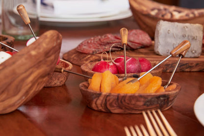 Olivewood condiment bowls of apricots and radishes on a set table with salami and an olivewood serving board