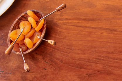 Overhead view of a single olivewood condiment bowl holding dried apricots with olivewood-handled cocktail picks