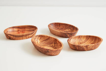Four shallow oval olivewood condiment bowls arranged on a white background, each about four inches across