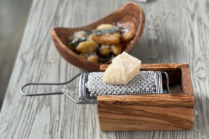Olivewood cheese grater on a weathered table with grated Parmigiano collected in the box and a wedge of cheese on the grating plate