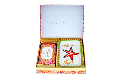 Amalfi Sunset gift box open, lid printed 'Everything starts as a dream', holding the Freesia and Summer Fruit body scrub beside a hand-painted Vietri ceramic soap dish with a red starfish, orange coral and a green dotted rim