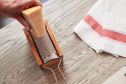 Hand grating a wedge of hard Italian cheese across the stainless plate of the olivewood box grater