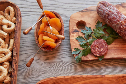 Olivewood condiment bowl of dried apricots beside taralli, salami and parsley on an olivewood serving board
