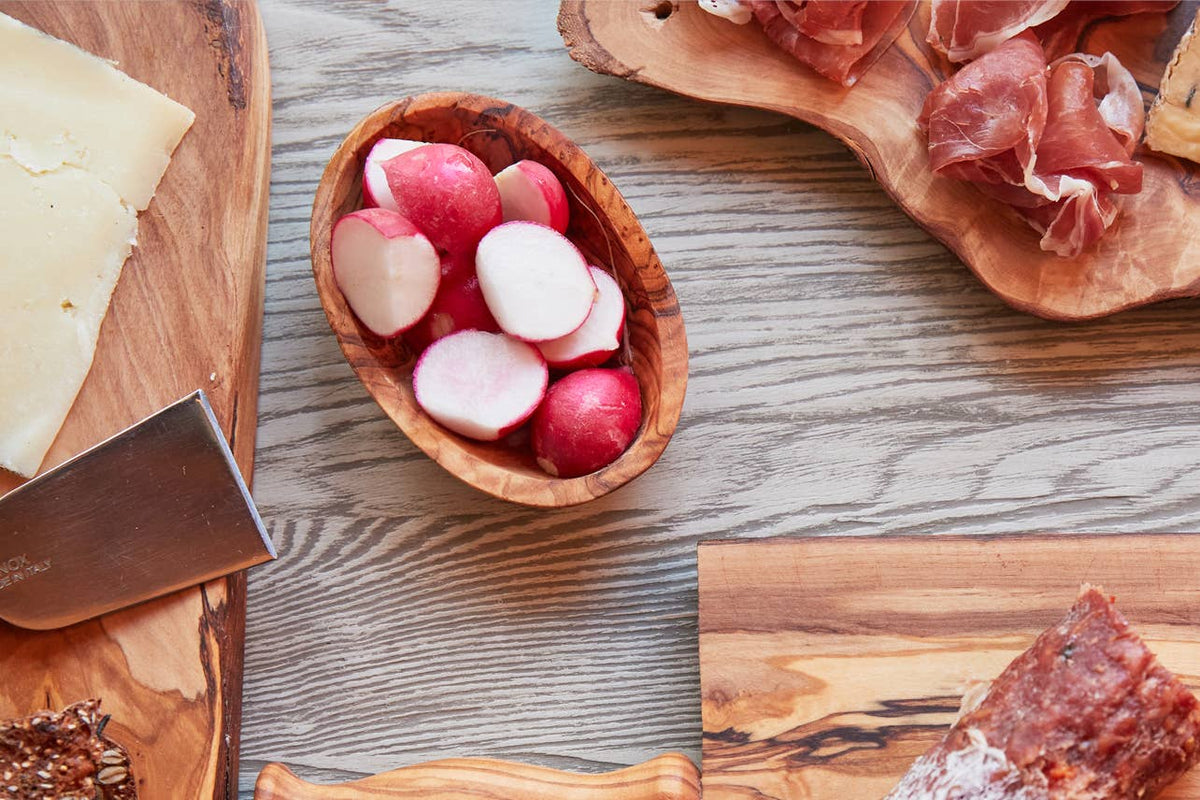 Olivewood condiment bowl of radishes on a charcuterie spread with prosciutto, cheese and an olivewood board