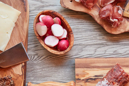 Olivewood condiment bowl of radishes on a charcuterie spread with prosciutto, cheese and an olivewood board