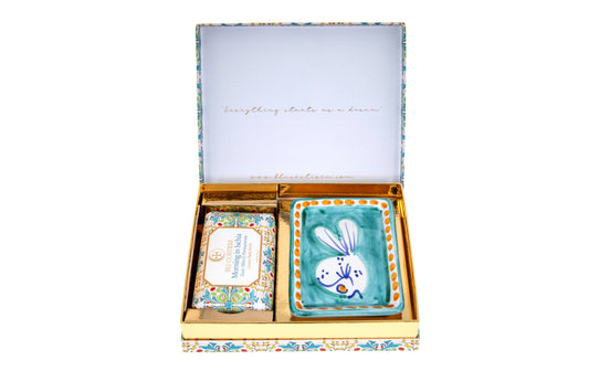 Blu Costiera Morning in Ischia gift box open, lid printed 'Everything starts as a dream', holding the Tonic Mint and Pomegranate body scrub beside a hand-painted Vietri ceramic soap dish with a white fish on turquoise and an orange dotted rim